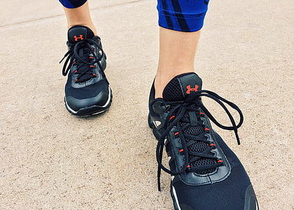 person wearing pair of black Under Armour lace-up sneakers on beige concrete thumbnail
