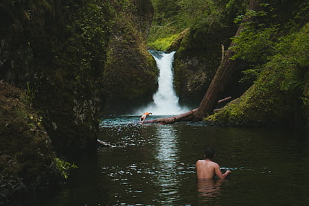 man submerged on body of water near waterfalls thumbnail