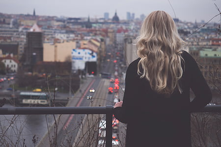 woman standing in front of black metal rail facing road and buildings thumbnail