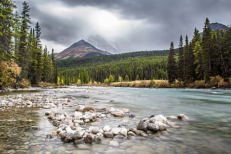 lake beside forest near mountain under cloudy sky thumbnail