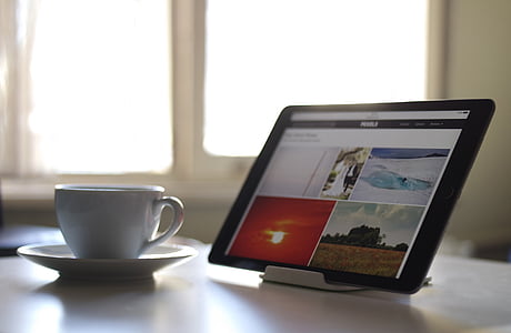 turned on tablet computer place beside white ceramic mug with saucer thumbnail
