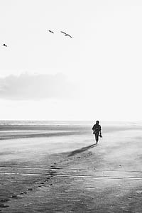 silhouette of person walking on sand beside shoreline thumbnail