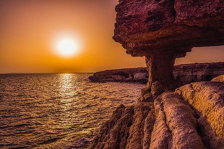 brown rock formation near body of water during sunset thumbnail