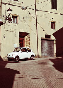 white 3-door hatchback parked beside brown building thumbnail