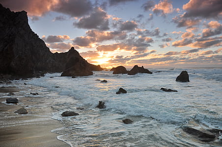body of water near rock formation under cloudy sky at daytime thumbnail