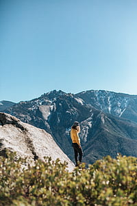 woman standing on rock mountain peak watching aerial view on trees and mountain under blue sky during daytime thumbnail