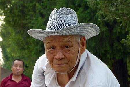 man wearing white collared shirt and white sunhat standing near green trees thumbnail