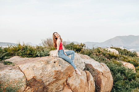 smiling woman sitting on top of rock surrounded with plants during daytime thumbnail