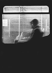 grayscale photo of man leaning on glass train window while sitting thumbnail