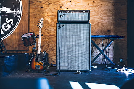 stratocaster guitar beside two gray amplifiers and electronic keyboard inside brown wooden room thumbnail