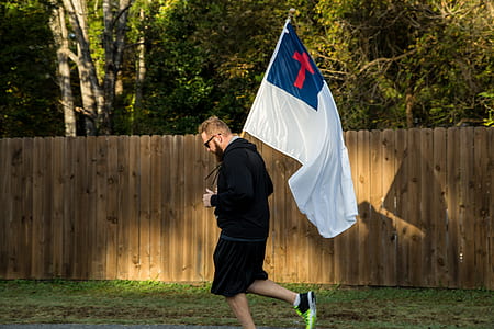 man wearing black hoodie carrying Christian flag thumbnail
