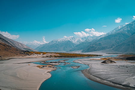 river next to gray sand and mountains under blue sky and white clouds thumbnail