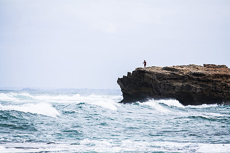 person on top of rock cliff surrounded by the body of water during daytime thumbnail
