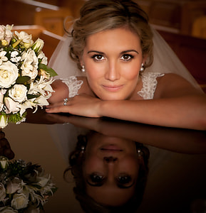 woman wearing wedding veil and dress leaning on black glass table holding a bouquet of flowers thumbnail