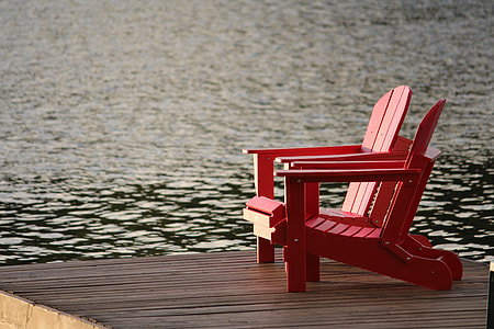 two red wooden armchairs on gray surface beside body of water thumbnail