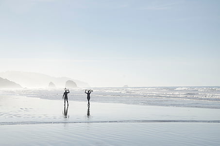 two people walking on seashore while carrying surfboards thumbnail