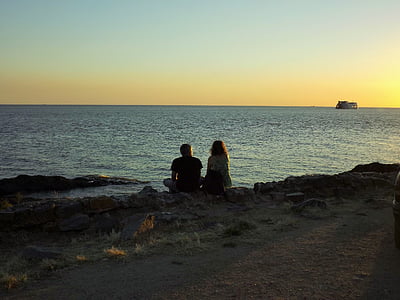 man and woman sitting on shore near body of water looking at distance thumbnail