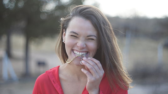 woman wearing red top biting gold necklace during daytime thumbnail