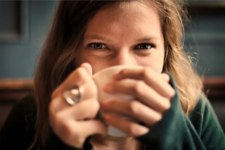 woman wearing green sweater sipping on white ceramic cup thumbnail