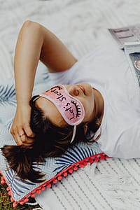 Joyful girl relaxing in bedroom - top view of brunette women in pink sleeping mask thumbnail