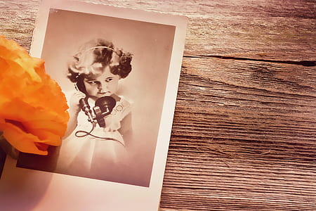 grayscale photo of girl holding phone on brown surface thumbnail