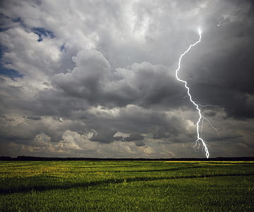 lightning on green field under cloudy sky during daytime thumbnail