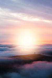 silhouette photography of person standing on mountain covered with clouds during golden hour thumbnail