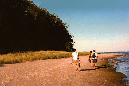 three person walking between mountain and body of water during daytime thumbnail