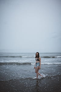 woman walking on shore under cloudy sky thumbnail
