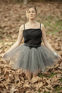 woman wearing black spaghetti strap mini dress kneeling on grass with dry leafs thumbnail