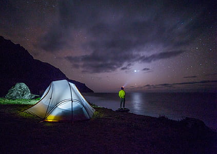man standing near body of water near lighted dome tent at night thumbnail
