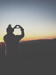 photo of person doing heart hand sign facing mountain thumbnail