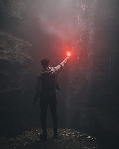 man holding red light standing front of cave wall thumbnail