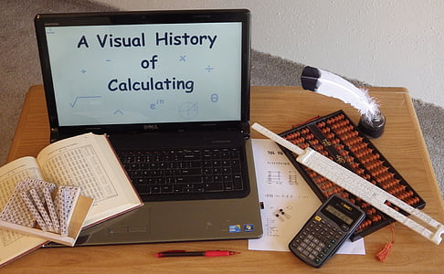 black and gray laptop, black abacus, scientific calculator, and book all on top of brown wooden desk thumbnail