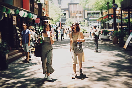 two women walking on road near shops thumbnail
