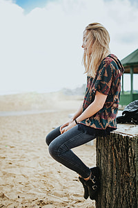 Beautiful blonde woman relaxing with a can of coke on a tree stump by the beach thumbnail