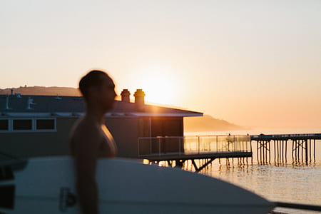 man carrying white surfboard near shore taken during golden hour thumbnail