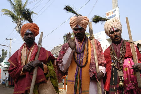 three men standing wearing turban holding wood sticks near coconut palm trees thumbnail