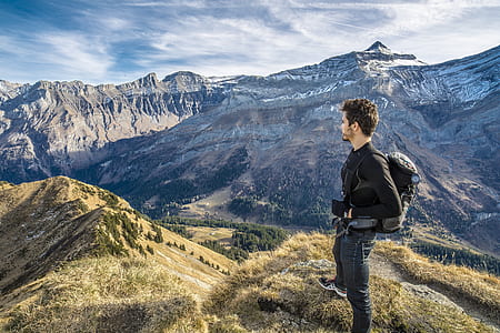 man wearin black jacket standing on a green mountain thumbnail