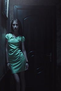 woman in green dress in front of brown wooden single-door thumbnail
