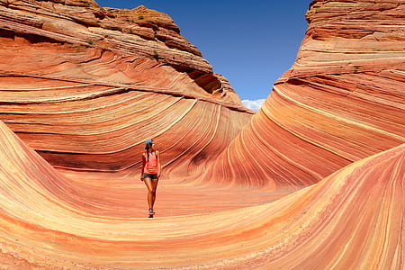 woman in pink tank top with black short shorts outfit walking near brown rock formation during daytime thumbnail