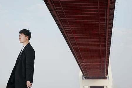 man wearing black coat standing under bridge during daytime thumbnail