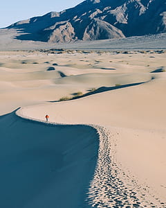 person walking along the desert near rocky mountains thumbnail
