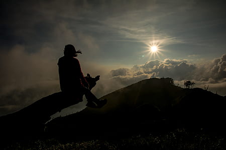 silhouette of person sitting on driftwood during daytime thumbnail