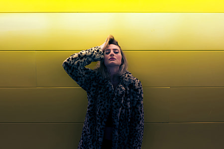 Woman wearing a coat standing by a yellow wall thumbnail