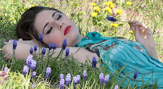 woman lying on grass holding purple grape hyacinth flower during daytime thumbnail