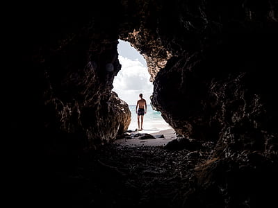 topless person standing at cave entrance near shore thumbnail