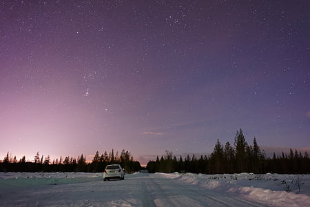 white vehicle traveling on snowy road near tree under starry skies thumbnail