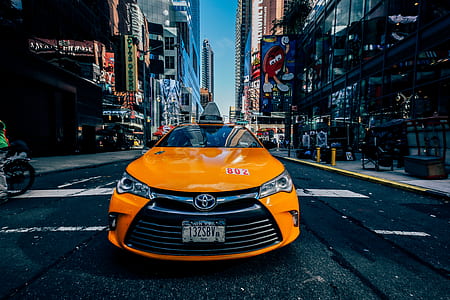 orange Toyota Corolla taxi cab on road in between buildings at daytime thumbnail