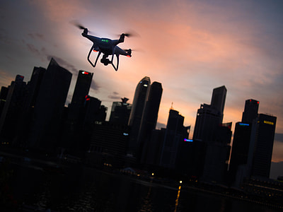 silhouette of quadcopter drone flying on air heading to buildings during golden hour thumbnail
